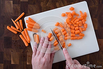 Womanâ€™s hands chopping baby carrots, white cutting board on wood butcher block Stock Photo